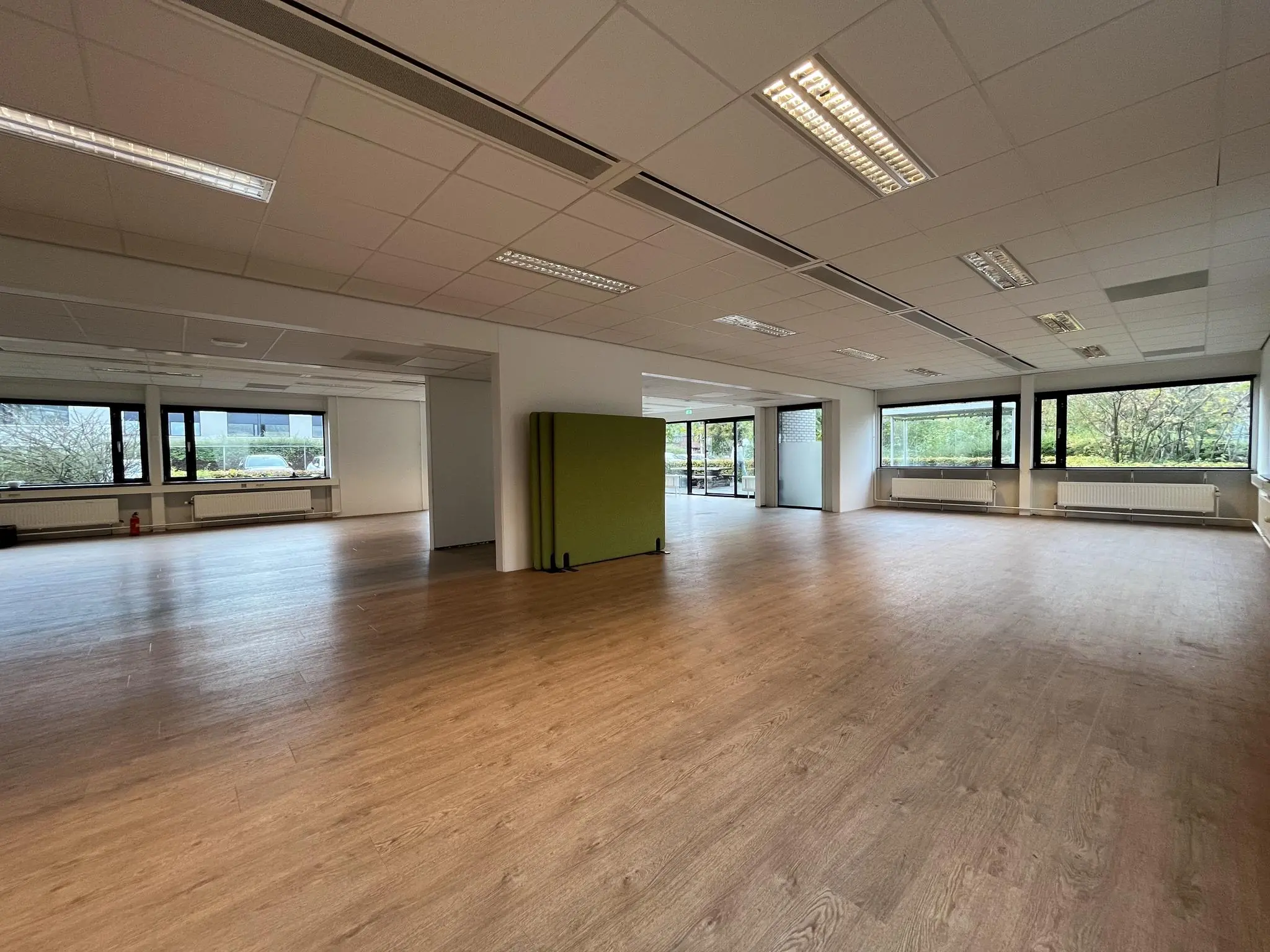 Leeg kantoorpand met houten vloer en grote ramen aan de Burgemeester Verderlaan.